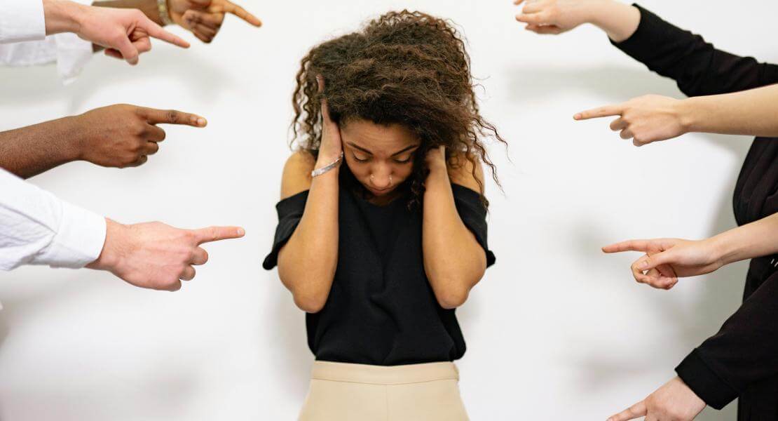 Femme au centre se couvre les oreilles et est pointée du doigt par des gens autour