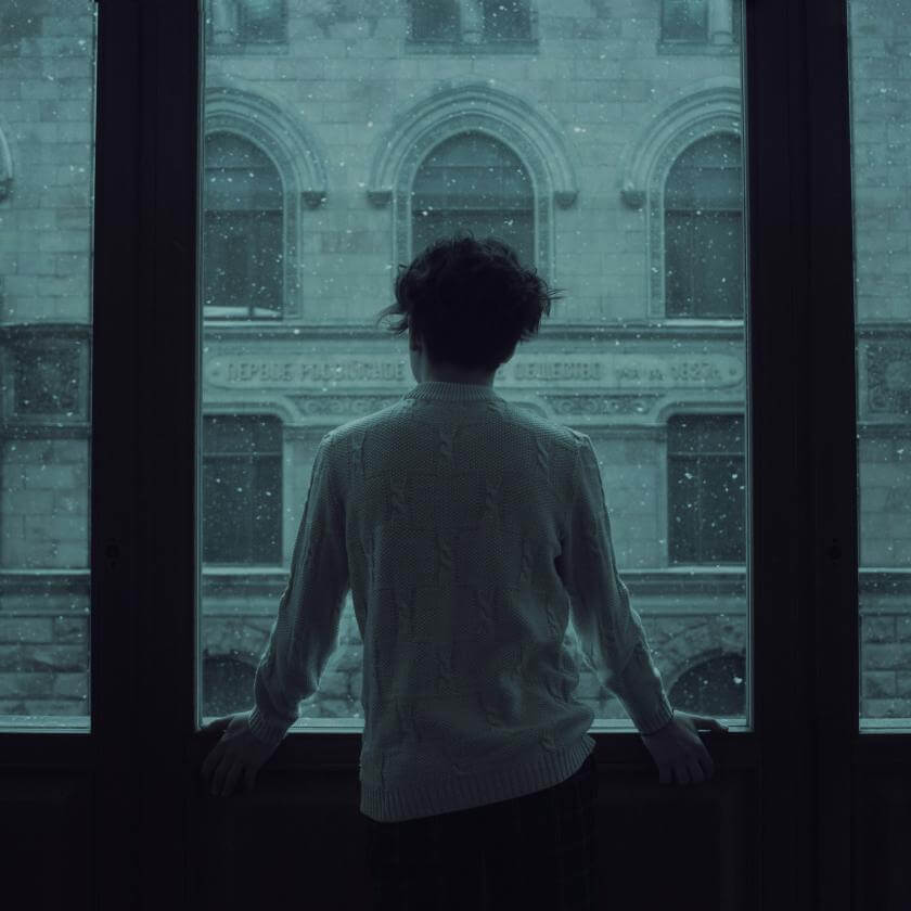 Young man standing in front of a window with a gray sky
