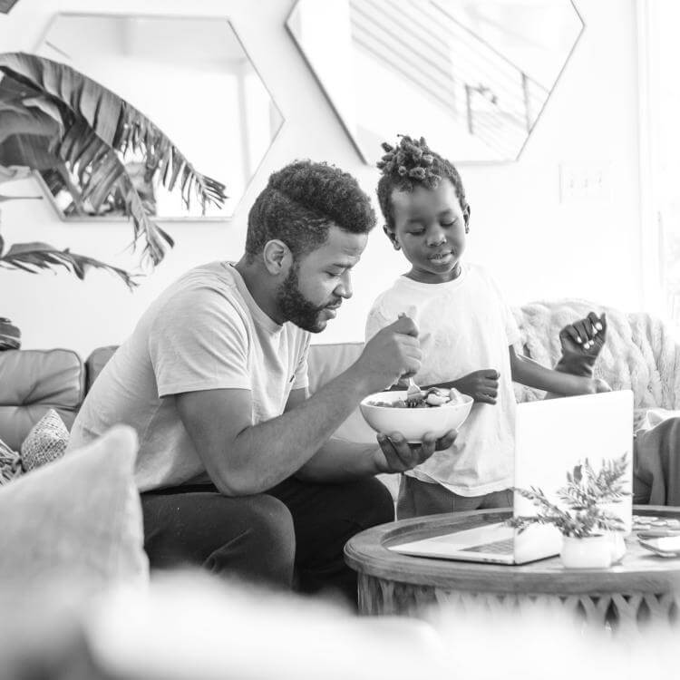 Un homme sur un divan tenant un bol de nourriture et deux enfants qui sourient